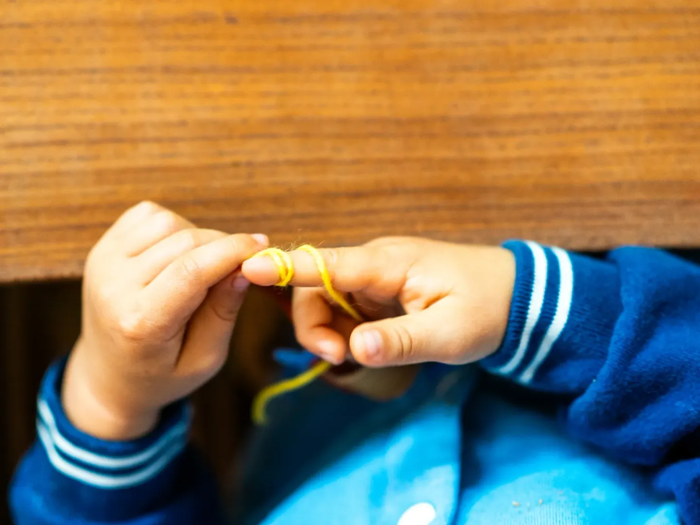 A child's hands threading wool at a timber table