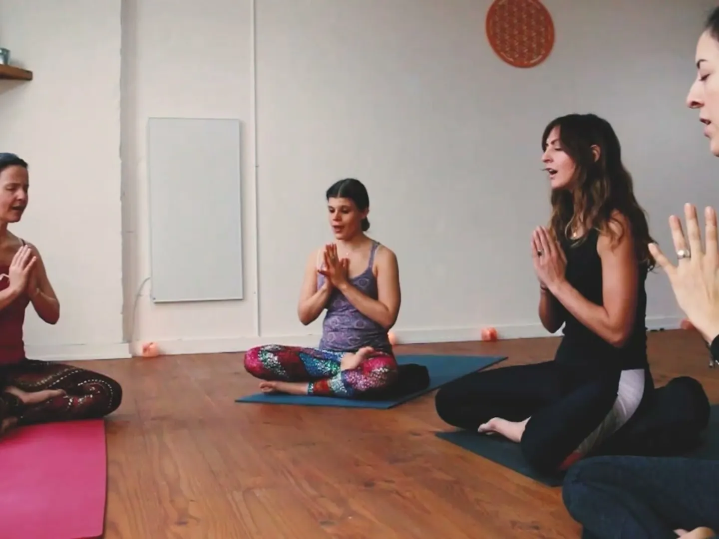 Small group seated on yoga mats, hands together, at the end of a session
