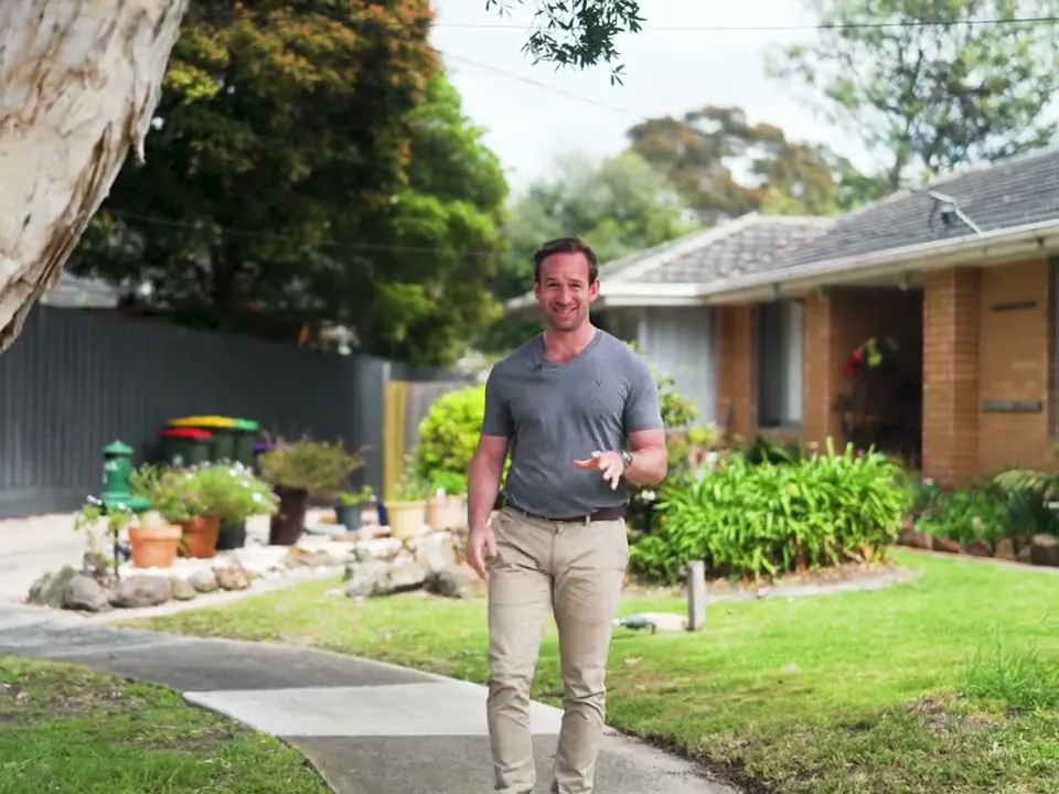 Real estate agent walking up a front garden, talking to camera