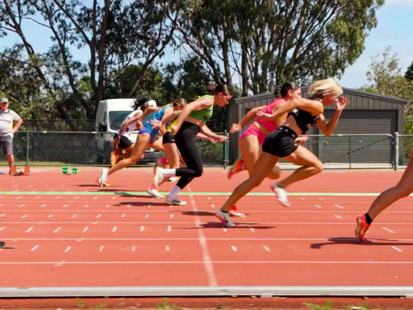 Sprinters exploding out of the blocks at a community athletics carnival