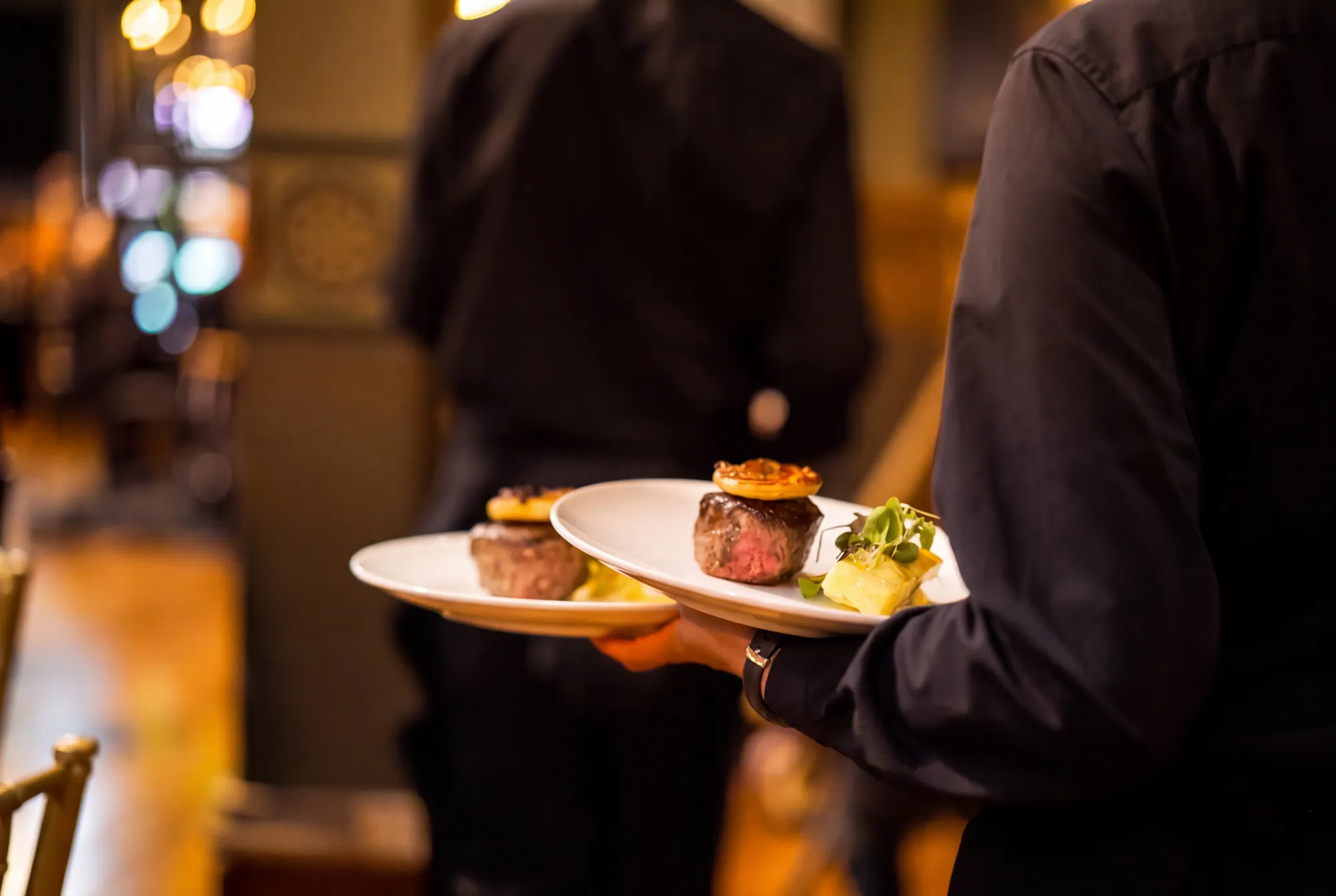 Waiter carrying two main courses through the dining room